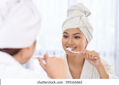 Young Vietnamese Woman Brushing Teeth In Front Of Mirror