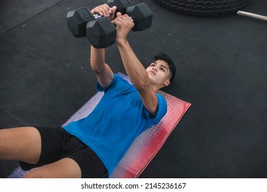 A Young Vigorous Asian Man Doing A Set Of Floor Chest Flys With A Pair Of Dumbbells At The Gym.