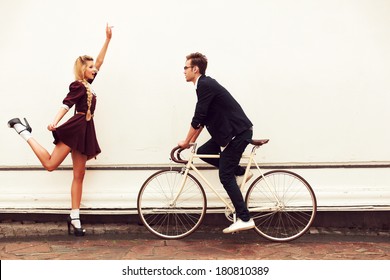 Young Vintage Hipster Pretty Couple Having Fun Outdoor In Summer On The Street In City With Cool Bicycle Behind White Wall. Man With Girl In Spring Urban Style