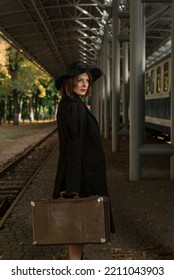 Young Vintage Lady With Retro Suitcase Waiting Train At Railroad Station. Full Length Portrait Of Middle-aged Woman In Coat And Hat