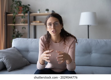 Young vlogger woman in glasses talking looks at camera record new videoblog share experience to internet audience while sit on sofa at home, participate in videocall, use modern tech, tutoring concept
