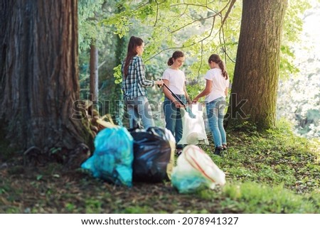 Young volunteers cleaning up the forest, they are putting trash in garbage bags, environmental protection concept