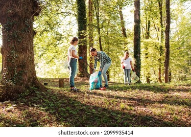 Young volunteers cleaning up the forest together, they are collecting trash and holding garbage bags