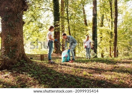 Young volunteers cleaning up the forest together, they are collecting trash and holding garbage bags