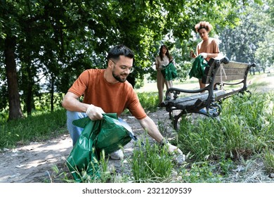 Young volunteers cleaning up park together, collecting trash and holding garbage bags. Responsible parents and friends cleaning public park from litter before children come to play outside in nature. - Powered by Shutterstock