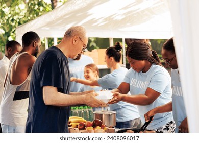 Young volunteers at local center giving complimentary nourishment to diverse group of homeless people benefiting from charitable food campaign. Charity workers share free meals to the hungry and poor.