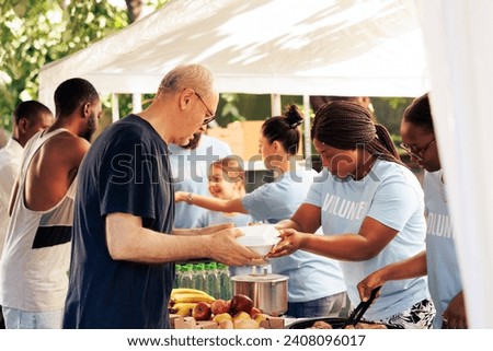 Young volunteers at local center giving complimentary nourishment to diverse group of homeless people benefiting from charitable food campaign. Charity workers share free meals to the hungry and poor.