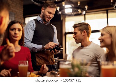 Young Waiter Accepting Credit Card Payment From His Guest Who Is Paying Restaurant Bill. 