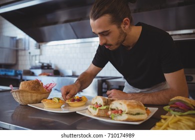 Young waiter arranging food in plate on counter at cafe - Powered by Shutterstock