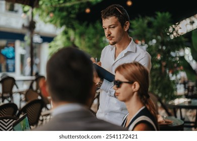 A young waiter assists businesspeople at an outdoor cafe, embodying customer service and hospitality in a casual setting. - Powered by Shutterstock