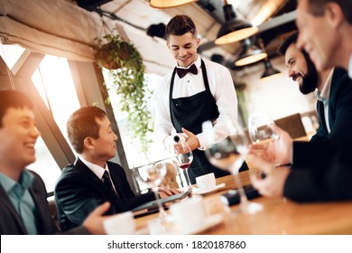 A young waiter pours wine into a glass to a Chinese businessman. Businessmen sit and chat in a restaurant while a waiter pours wine. - Shutterstock ID 1820187860