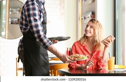 Young Waiter Serving Tasty Dish To Client In Restaurant