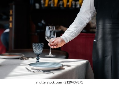 A young waiter in a stylish uniform is engaged in serving the table in a beautiful gourmet restaurant close-up. Table service in the restaurant.