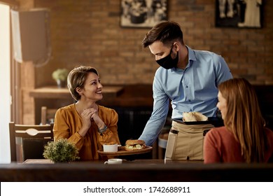 Young waiter wearing protective face mask while serving food to his guests in a restaurant.  - Shutterstock ID 1742688911
