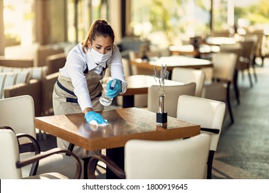 Young waitress disinfecting tables while wearing protective face mask ad gloves due to coronavirus epidemic. 
