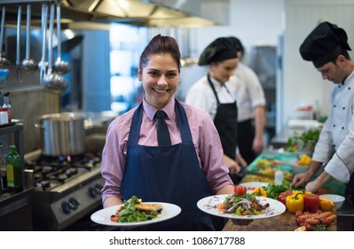 young waitress presenting dishes of tasty meals in commercial kitchen - Powered by Shutterstock