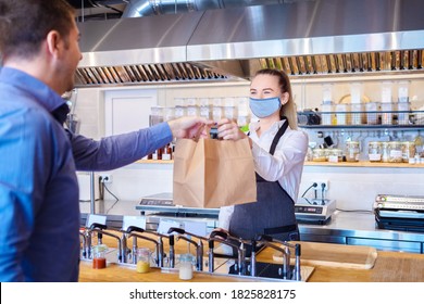 Young waitress waring protective face mask and apron serving customer at counter in small restaurant - Small business and entrepreneur concept with woman owner in eatery with takeaway service delivery - Shutterstock ID 1825828175