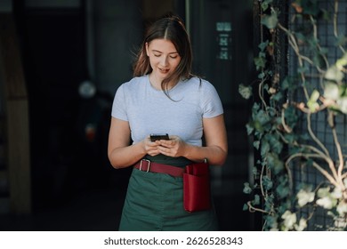 Young waitress wearing an apron and engaging with a smartphone app while working in a bustling restaurant environment