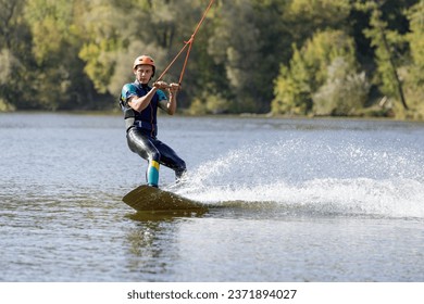 Young wakeboarder surfing along the river. Young man performing heelside edge surfing - Powered by Shutterstock