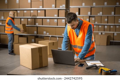 Young warehouse employee at work, he is checking orders on a laptop - Powered by Shutterstock