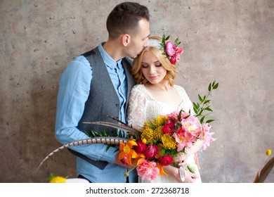 Young Wedding Couple Against Texture Wall And Table With Small Cakes