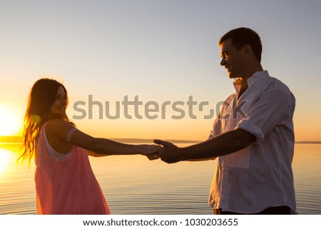 Young wedding couple is holding hands and spinning in the water on summer beach. Sunset over the sea. Romantic love story. Man and woman in holiday honeymoon trip. Happy emotions.