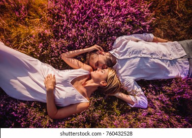 Young Wedding Couple Lies On The Golden Field With Violet Flowers