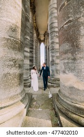 Young wedding couple posing between rows of antique building columns