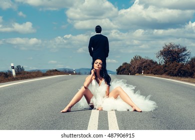 Young Wedding Happy Couple Of Sexy Girl With Brunette Hair And Pretty Face In White Bride Dress And Handsome Man In Black Groom Suit On Road Way On Cloudy Blue Sky Nature Background