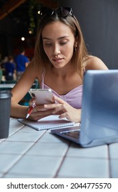 Young Well Dressed Asian Woman Sitting At Table, Using Her Smartphone. Beautiful Lady Surfing Internet On Cell Phone At Cafe, Chatting Online.