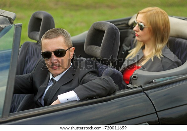 Young well dressed man and\
woman couple well dressed, wearing sunglasses in cabriolet\
convertible car