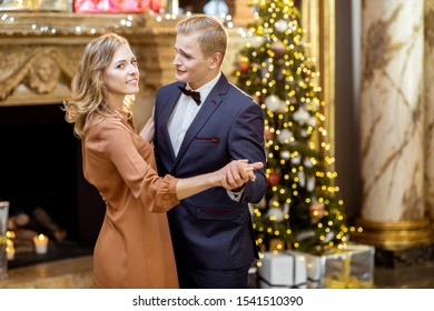 Young well-dressed couple dancing near the christmas tree during the New Year celebration at the beautifully decorated home - Shutterstock ID 1541510390