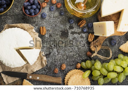 Young white cheese, a new recipe for cheese with fenugreek, a hard chopped Parmesan on a gray stone background with blueberries, nuts, green grapes, honey. Top view. Selective focus..