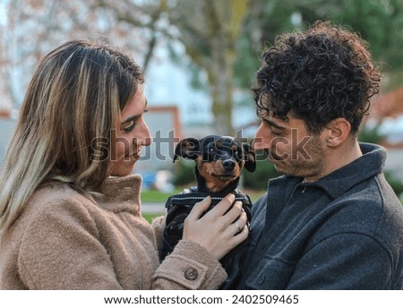 Young white couple holding a dog in a park, looking at it tenderly. Dog looking at the horizon