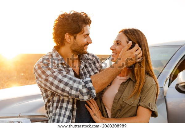 Young white couple hugging and smiling while\
standing by car on field