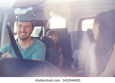 Young White Family Of Four In Their Car, Mum Turning To Speak To Kids, Seen Through Front Windscreen