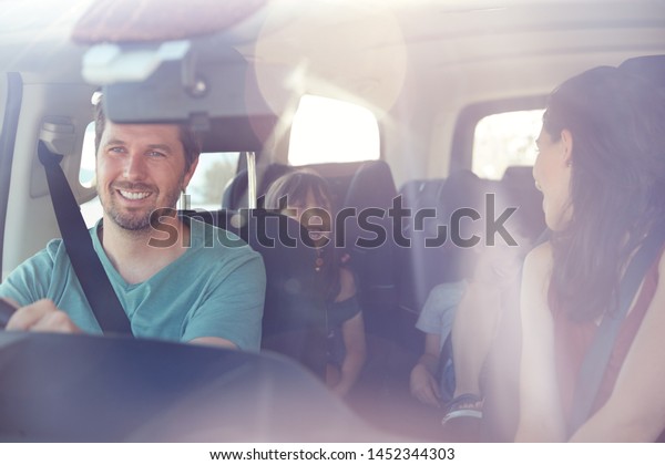 Young white family of four\
in their car, mum turning to speak to kids, seen through front\
windscreen