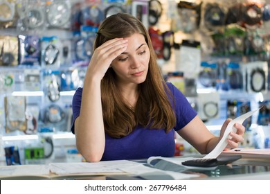 Young White Female Entrepreneur Running A Small Business And Working In Computer Shop, Checking Bills And Invoices With Worried Expression