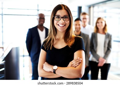 Young White Female Executive Standing In Front Of Colleagues With Arms Crossed And Smiling