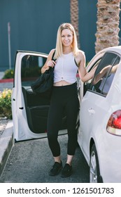 Young White Girl Exits Her Car With Her Gym Bag And Dressed In Workout Wear.  Happy Millennial