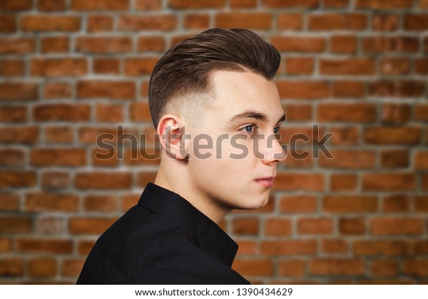Young white guy\
with pompadour hairstyle dressed in black shirt with a serious face\
on brick wall background