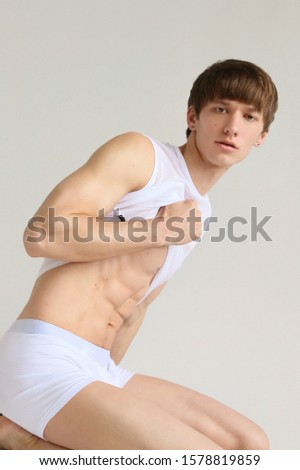 young white handsome guy in a white t-shirt and shiny white underwear  posing on camera on a white background on the floor
