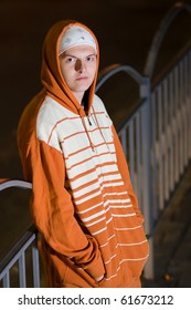 Young White Hip Hop Gangster In Hoodie Coat And Headband Hustling On Street Corner At Night. Gang Member Selling Drugs On The Street. Street Wear Fashion Male Model Guy