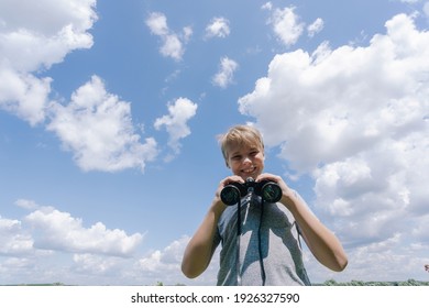 Young white kid looking at camera holding black vintage binoculars in hands isolated on sunny summer bright blue sky background. Portrait of cute happy smiling and laughing boy - Powered by Shutterstock