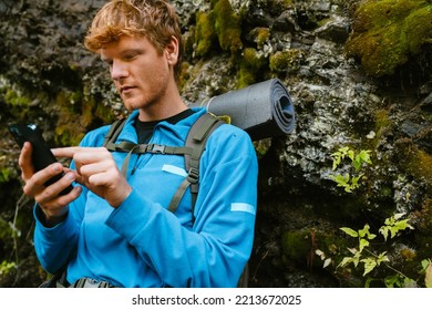 Young white man with backpack using cellphone while hiking in forest
