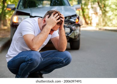 Young White Man Driver In Car Accident And Holding His Head Near Broken Car On The Road After A Car Accident. Caucasian Man Facepalm Holding Head Injury After Accident