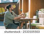 A young white man on a street food court in a modern urban space. Fast food, street food. A handsome guy is sitting at an outdoor cafe table.