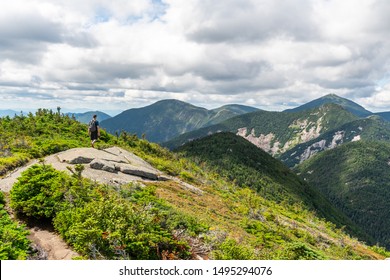Young white man walking on top of a mountain with a beautiful view in the background on a sunny day. Inspiring, adventurer. Shot on the Ghotics Mountain, Adirondacks National Park, NY, USA. 