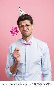 Young White Man Wearing Party Cone Posing With Flower Wind Spinner Isolated Over Pink Background