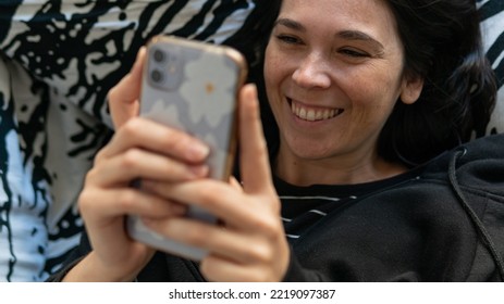 Young White Spanish Woman Smiling And Having Fun With The Phone On The Hands, Close Up